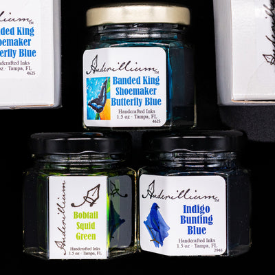 An overhead view of 3 Anderillium ink bottles in a pyramid form with 2 boxes by their sides.