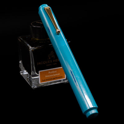 AP Limited Editions Proplyd Aqua Fountain Pen capped, leaning against an ink bottle. 