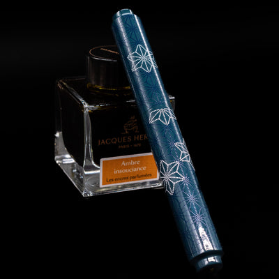 AP Limited Editions Sakura Lacquer Art Fountain Pen - Snowflakes Blue  capped, leaning against an ink bottle. 