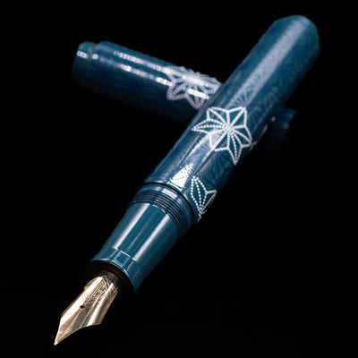 AP Limited Editions Sakura Lacquer Art Fountain Pen - Snowflakes Blue laying across its own cap, crossed, with a focus on the nib.