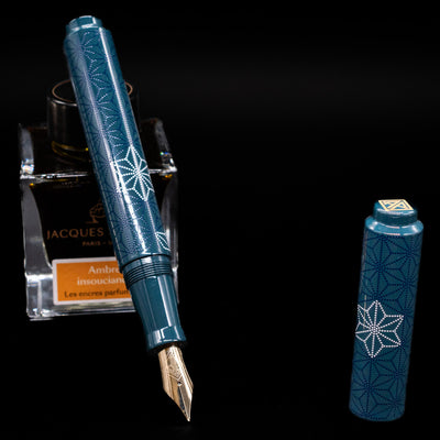 AP Limited Editions Sakura Lacquer Art Fountain Pen - Snowflakes Blue leaning on an ink bottle uncapped showcasing the detailing on the nib.