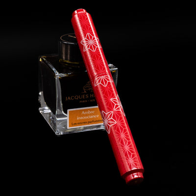 AP Limited Editions Sakura Lacquer Art Fountain Pen - Snowflakes Red capped, leaning against an ink bottle. 