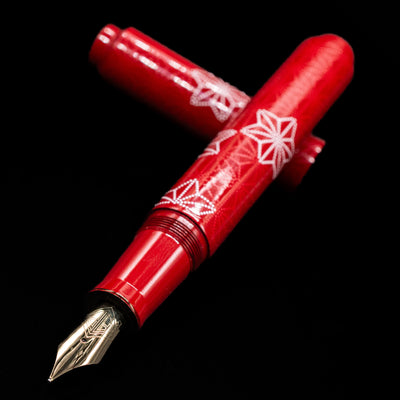 AP Limited Editions Sakura Lacquer Art Fountain Pen - Snowflakes Red laying across its own cap, crossed, with a focus on the nib.
