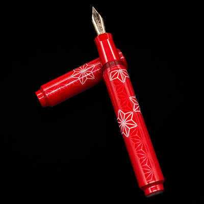 AP Limited Editions Sakura Lacquer Art Fountain Pen - Snowflakes Red laying on top of its cap in a crossed position showing full view of the entire uncapped pen.