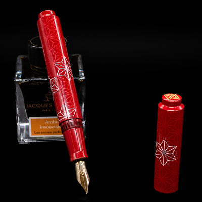AP Limited Editions Sakura Lacquer Art Fountain Pen - Snowflakes Red  leaning on an ink bottle uncapped showcasing the detailing on the nib.