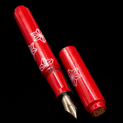 A full view of the AP Limited Editions Sakura Lacquer Art Fountain Pen - Snowflakes Red uncapped, with its cap laying next to the pen. 