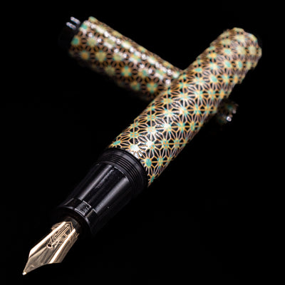 AP Limited Editions Sakura Lacquer Art Fountain Pen - Teal Stars laying across its own cap, crossed, with a focus on the nib.