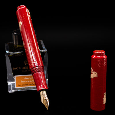 AP Limited Editions Sakura Lacquer Art Fountain Pen - Year of the Rabbit leaning on an ink bottle uncapped showcasing the detailing on the nib.