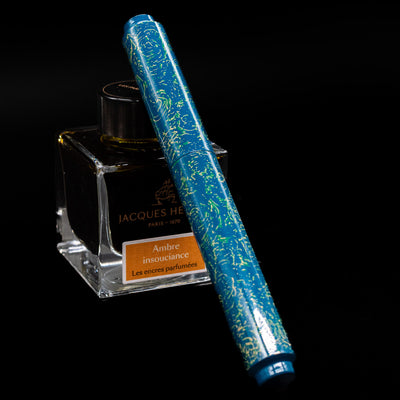 AP Limited Editions Urushi Lacquer Art Fountain Pen - Blue Bliss capped, leaning against an ink bottle. 
