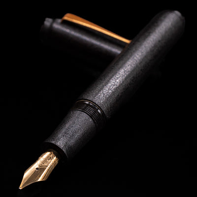 AP Limited Editions Urushi Lacquer Art Fountain Pen - Ishiji Black & Gold laying across its own cap, crossed, with a focus on the nib.