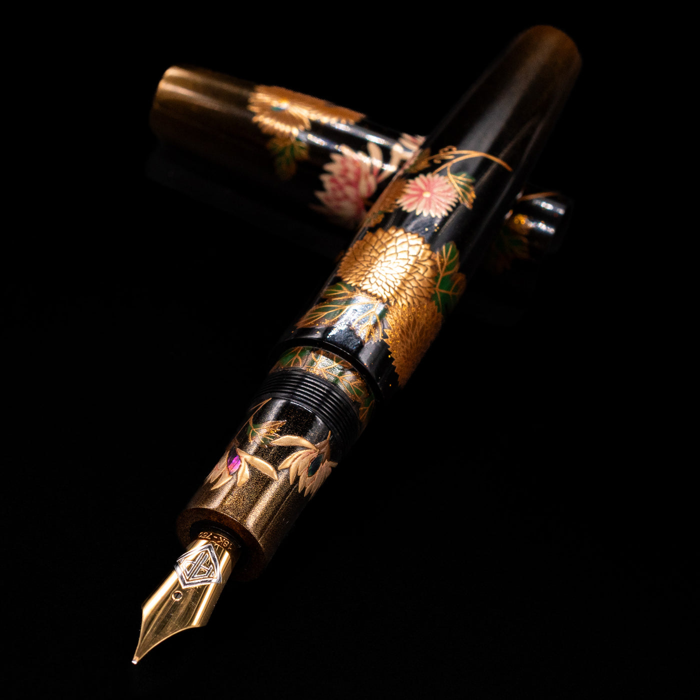 AP Limited Editions Writer Maki-e Fountain Pen - Chrystanthemum (Prototype) laying across its own cap, crossed, with a focus on the nib.