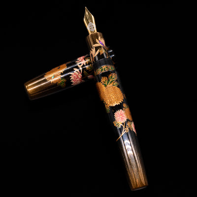 AP Limited Editions Writer Maki-e Fountain Pen - Chrystanthemum (Prototype) laying on top of its cap in a crossed position showing full view of the entire uncapped pen.
