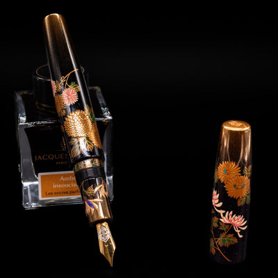 AP Limited Editions Writer Maki-e Fountain Pen - Chrystanthemum (Prototype) leaning on an ink bottle uncapped showcasing the detailing on the nib.