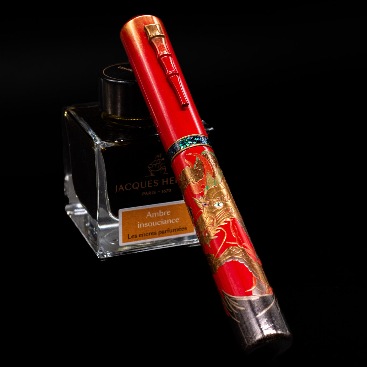 AP Limited Editions Writer Maki-e Fountain Pen - The Celebrated Dragon capped, leaning against an ink bottle. 