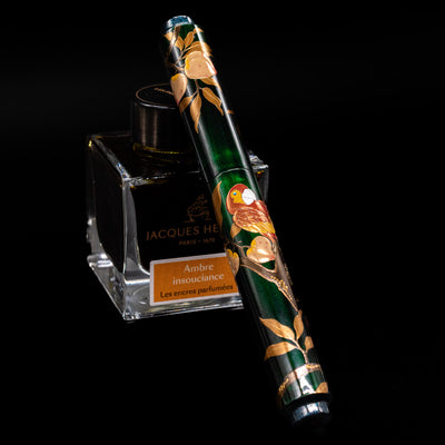 AP Limited Editions Writer Maki-e Fountain Pen - The Parrot with Peaches capped, leaning against an ink bottle. 