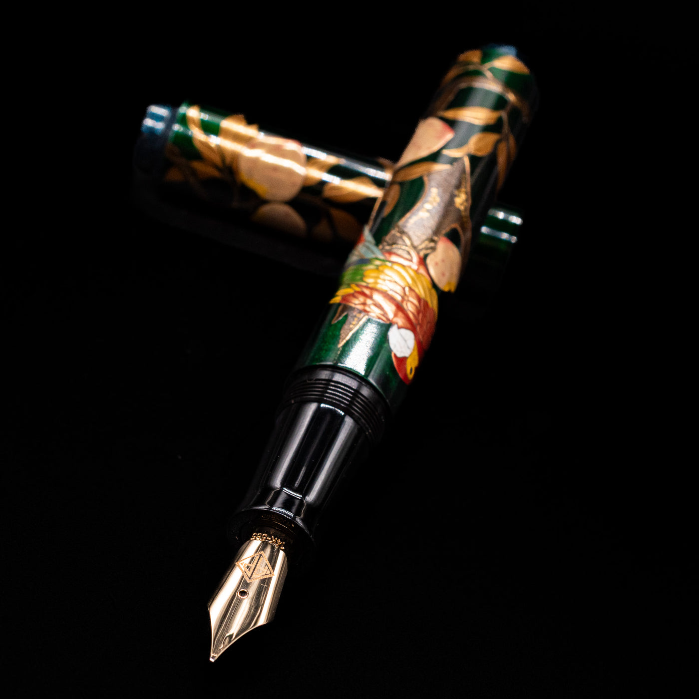 AP Limited Editions Writer Maki-e Fountain Pen - The Parrot with Peaches laying across its own cap, crossed, with a focus on the nib.