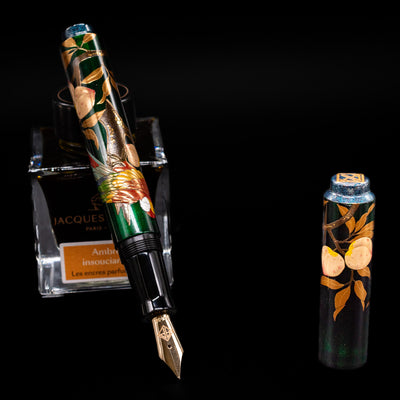 AP Limited Editions Writer Maki-e Fountain Pen - The Parrot with Peaches leaning on an ink bottle uncapped showcasing the detailing on the nib.