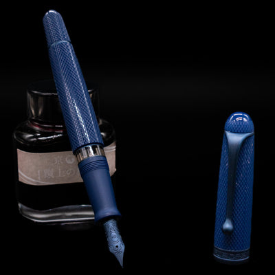 Aurora 88 Blue Mamba Fountain Pen leaning on an ink bottle uncapped showcasing the detailing on the nib.
