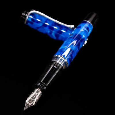 Aurora Optima Auroloide Blue & Chrome fountain pen and cap crossed, with focus on the engraved nib and the vibrant marbled blue resin.