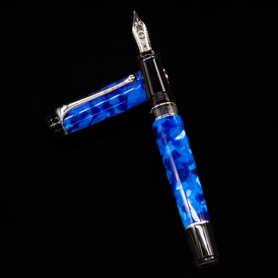 Aurora Optima Auroloide Blue & Chrome fountain pen and cap arranged in a crossed position, highlighting the elegant marbled blue finish, engraved cap band, and rhodium-plated clip.