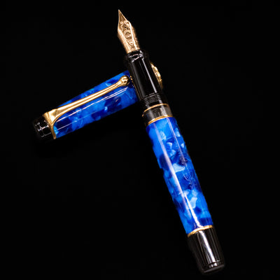 Aurora Optima Auroloide Blue & Gold fountain pen and cap arranged in a crossed position, highlighting the elegant marbled blue finish, engraved cap band, and gold-plated clip.