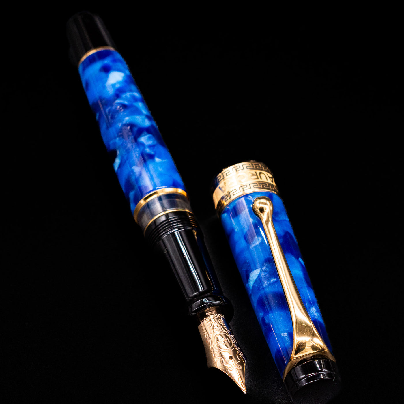Aurora Optima Auroloide Blue & Gold fountain pen displayed uncapped, revealing the marbled blue resin barrel, gold-plated grip section, and engraved gold nib.