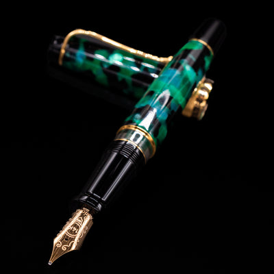 Aurora Optima Auroloide Emerald Green fountain pen and cap crossed, with focus on the engraved gold nib and the deep marbled green resin.
