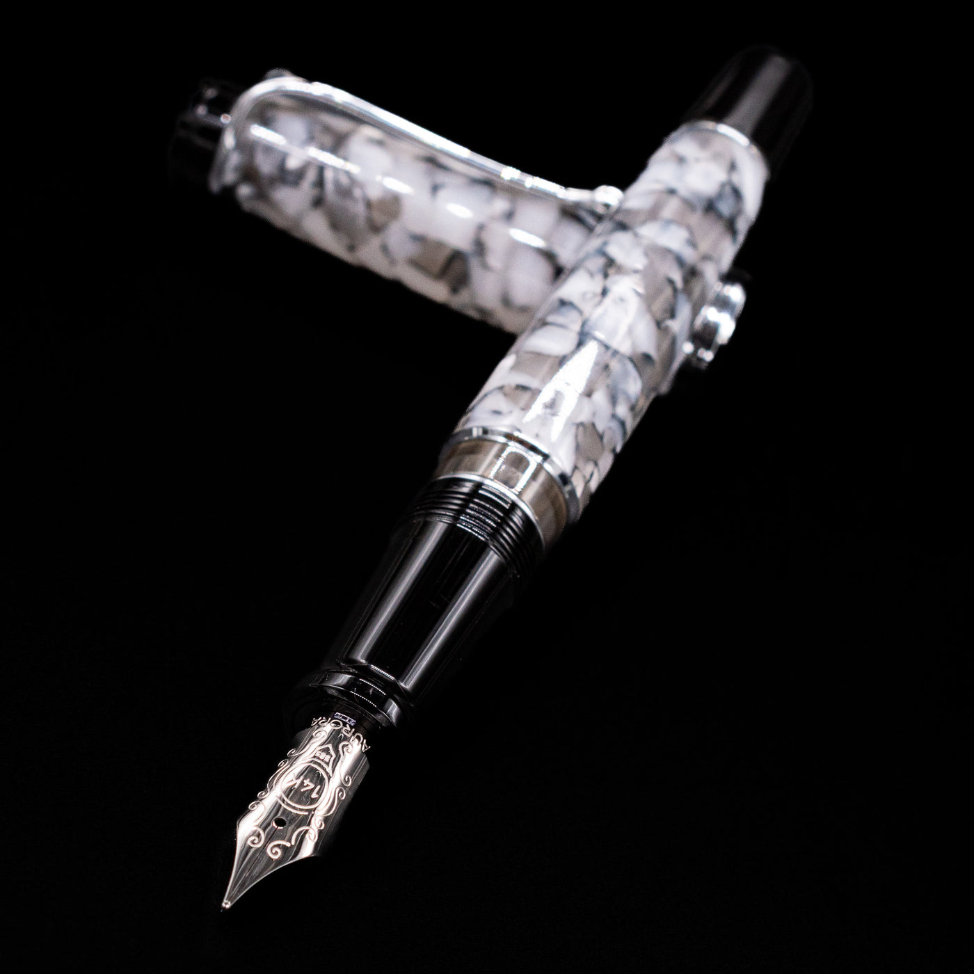 Aurora Optima Auroloide Nero Perla fountain pen and cap crossed, with focus on the engraved nib and the sleek marbled black-and-grey resin.