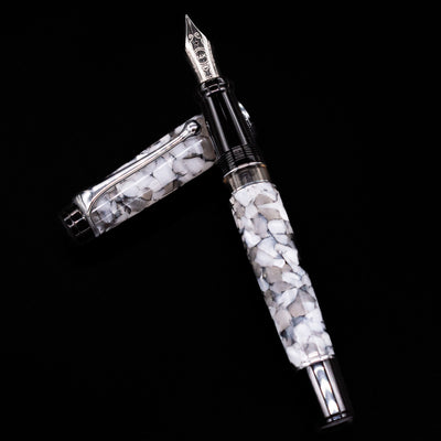 Aurora Optima Auroloide Nero Perla fountain pen and cap arranged in a crossed position, highlighting the marbled black-and-grey resin, engraved cap band, and rhodium-plated clip.
