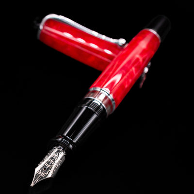 Aurora Optima Auroloide Rossa fountain pen and cap crossed, with focus on the engraved gold nib and the striking marbled red resin.