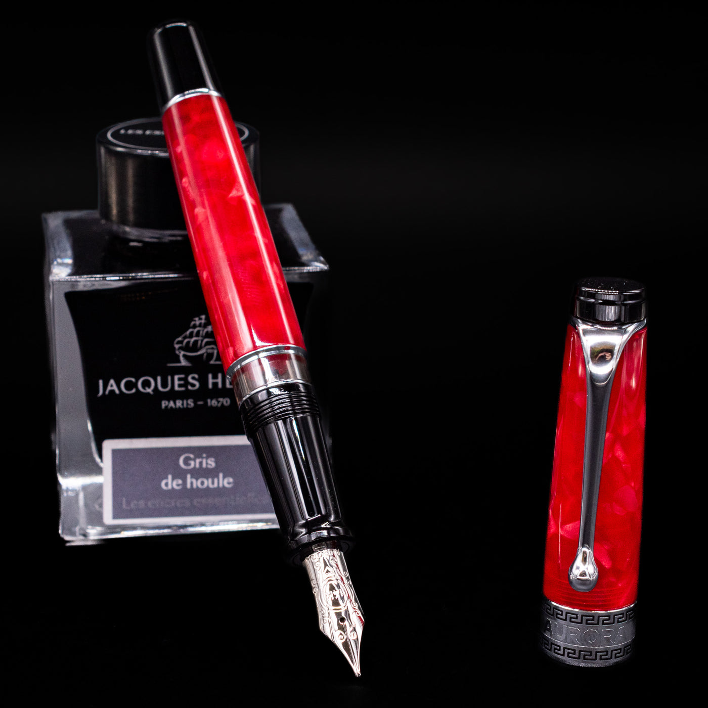 Aurora Optima Auroloide Rossa fountain pen displayed uncapped, leaning on an ink bottle to reveal its rhodium-plated 14k nib. The rich marbled red resin barrel is complemented by a matching cap and silver accents.