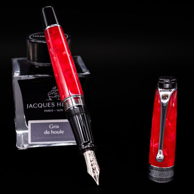 Aurora Optima Auroloide Rossa fountain pen displayed uncapped, leaning on an ink bottle to reveal its rhodium-plated 14k nib. The rich marbled red resin barrel is complemented by a matching cap and silver accents.