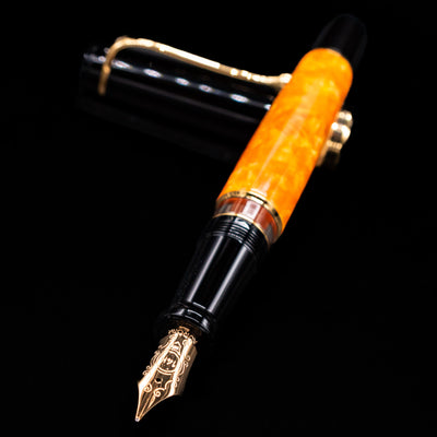 Aurora Optima O Sole Mio fountain pen and cap crossed, with focus on the engraved gold nib and the vivid marbled orange barrel.