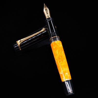 Aurora Optima O Sole Mio fountain pen and cap arranged in a crossed position, showcasing the striking combination of black resin, marbled orange resin, decorative cap band, and gold-plated clip.