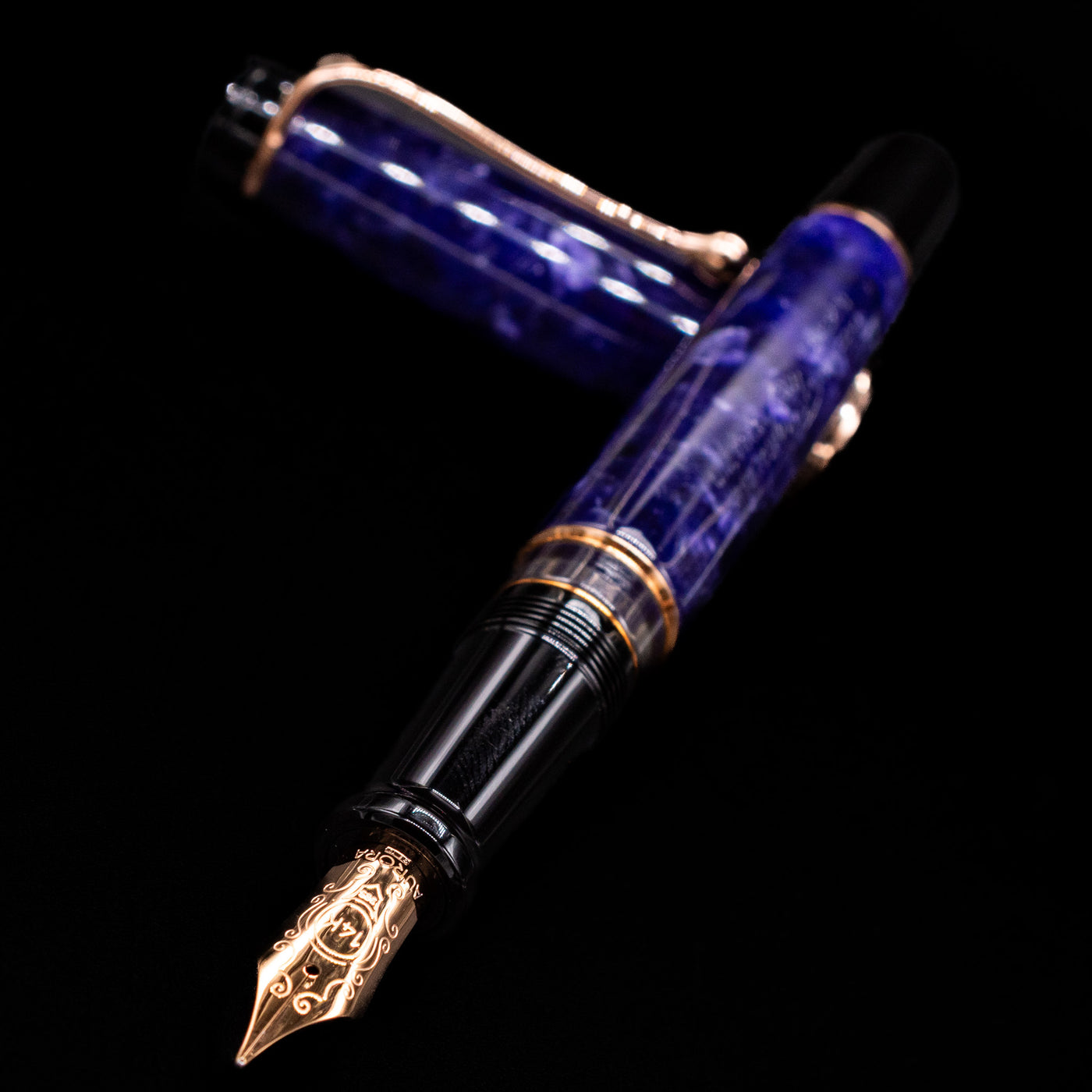 Aurora Optima Viola fountain pen and cap crossed, with focus on the engraved nib and the vibrant marbled purple resin.