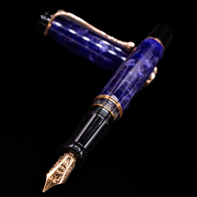 Aurora Optima Viola fountain pen and cap crossed, with focus on the engraved nib and the vibrant marbled purple resin.