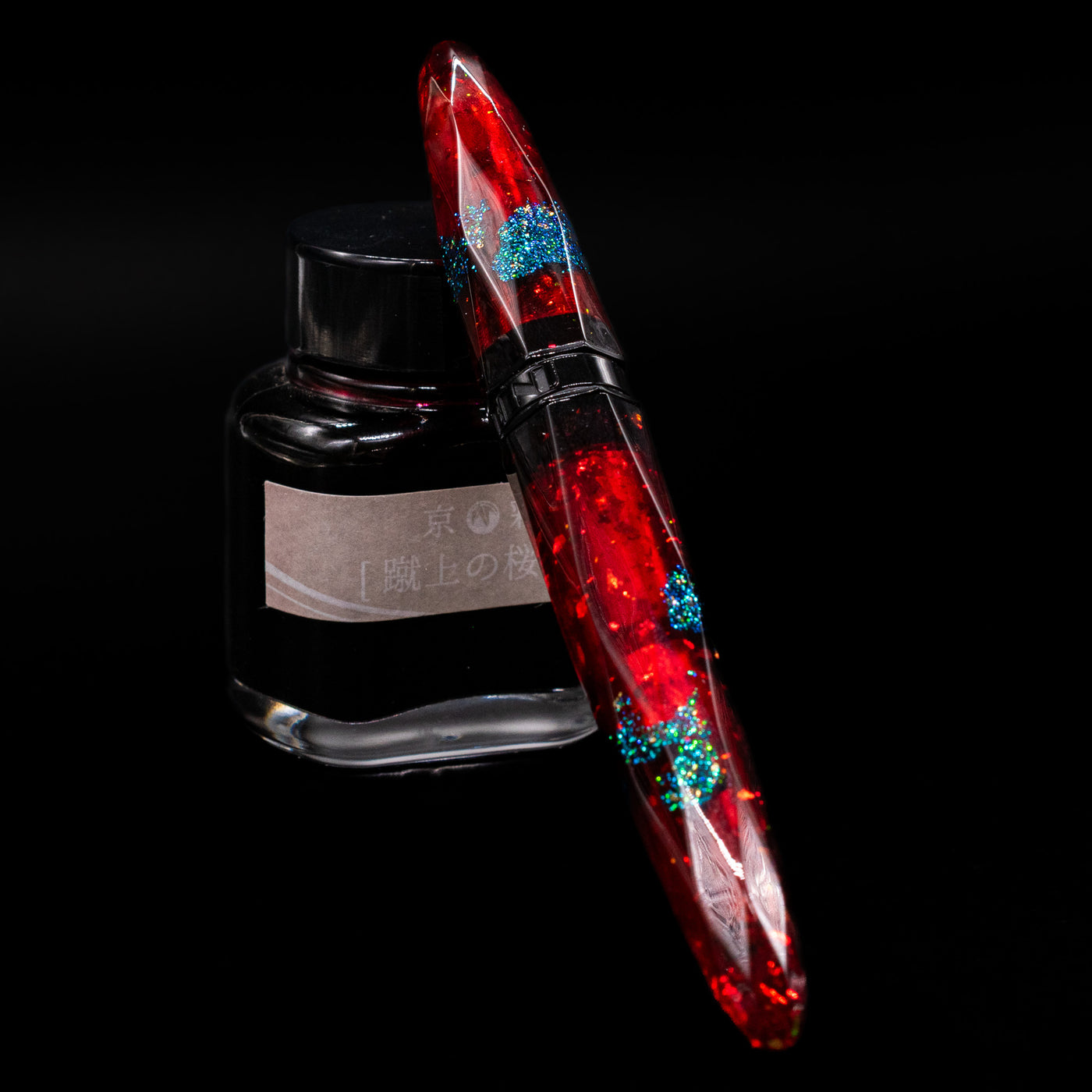BENU Briolette Fountain Pen - Ruby Forest capped, leaning against an ink bottle. 
