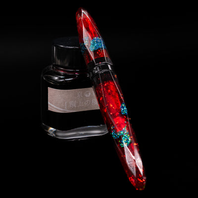 BENU Briolette Fountain Pen - Ruby Forest capped, leaning against an ink bottle. 