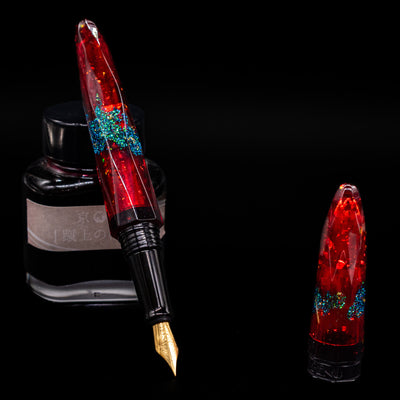 BENU Briolette Fountain Pen - Ruby Forest leaning on an ink bottle uncapped showcasing the detailing on the nib.