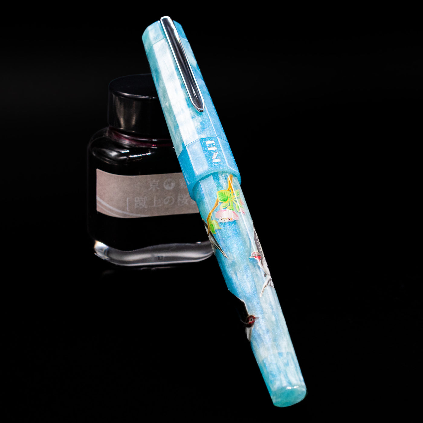 BENU Euphoria Limited Edition Fountain Pen - Swallow’s Song capped, leaning against an ink bottle. 
