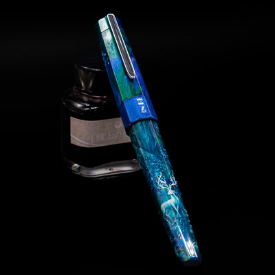 BENU Euphoria White Stag Fountain Pen capped, leaning against an ink bottle. 