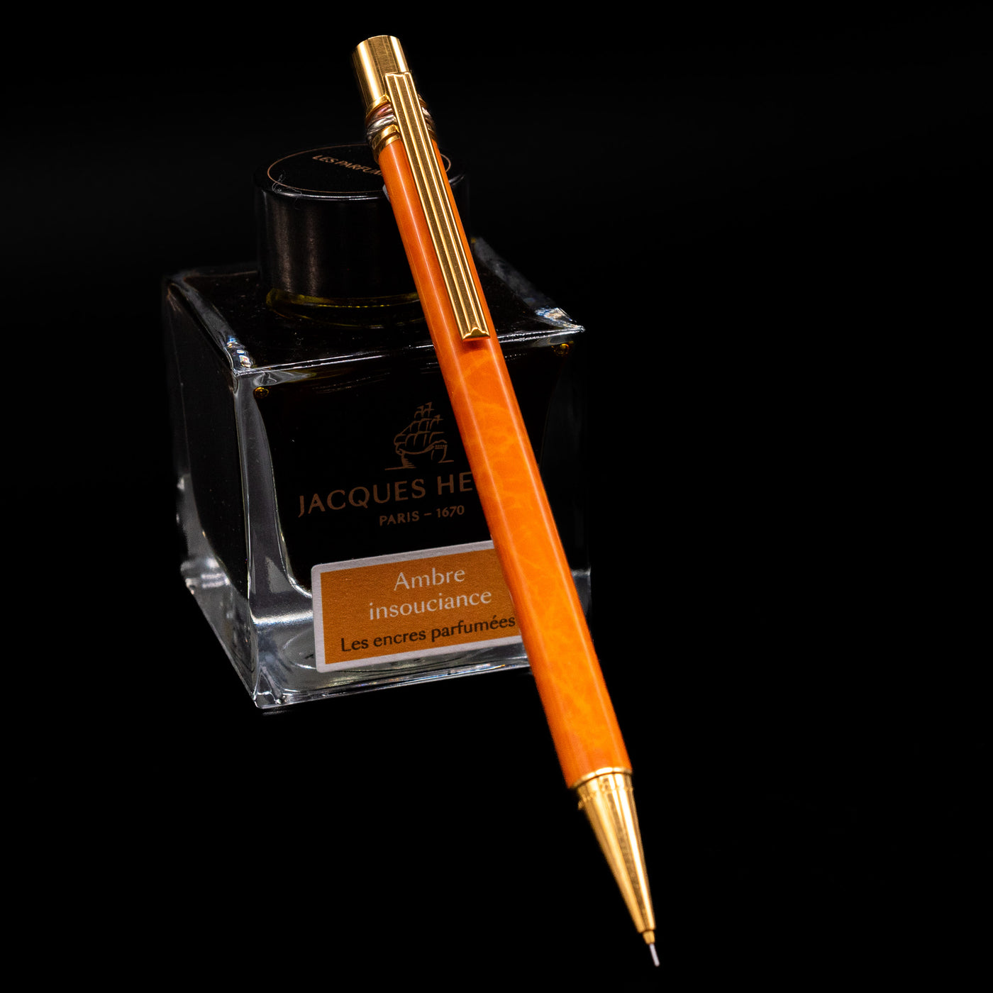 Cartier Trinity Orange Mechanical Pencil - Preowned leaning against an ink bottle.