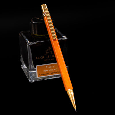 Cartier Trinity Orange Mechanical Pencil - Preowned leaning against an ink bottle.