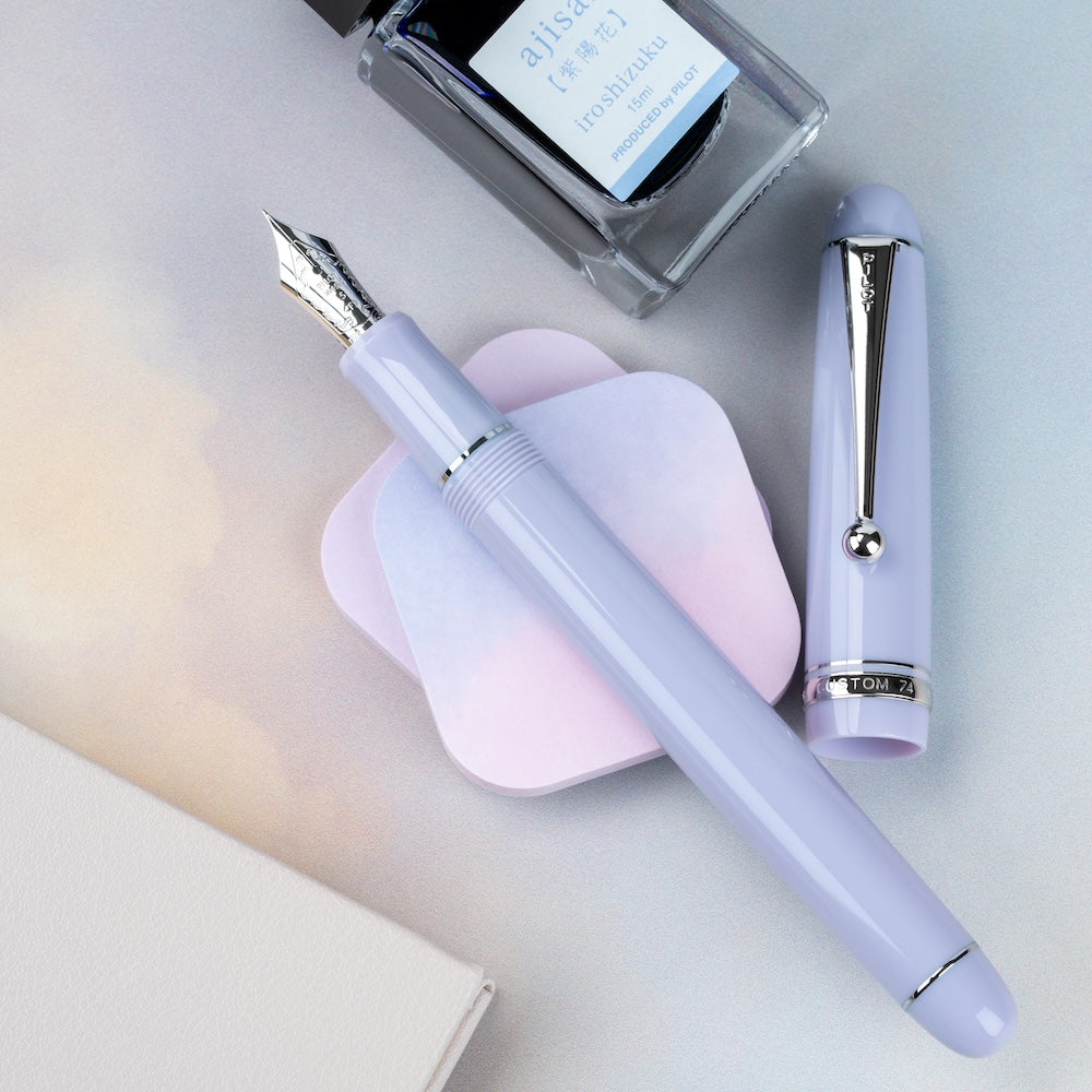Purple fountain pen with cap and ink bottle on a light surface