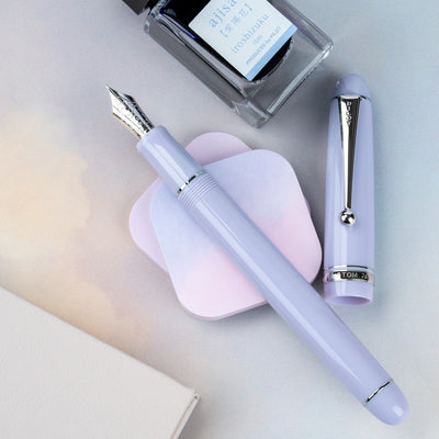 Purple fountain pen with cap and ink bottle on a light surface
