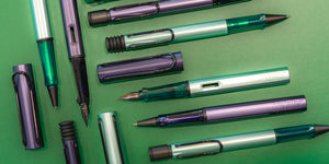 LAMY Al-Star Dark Dusk fountain pen shown capped, resting diagonally against a matching ink bottle. The pen features a deep smoky violet aluminum body and a black clip, with soft lighting highlighting its sleek, modern design.