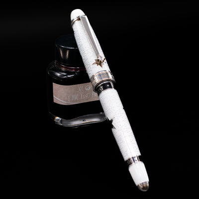 David Oscarson Black Star & Frost Fountain Pen capped, leaning against an ink bottle. 