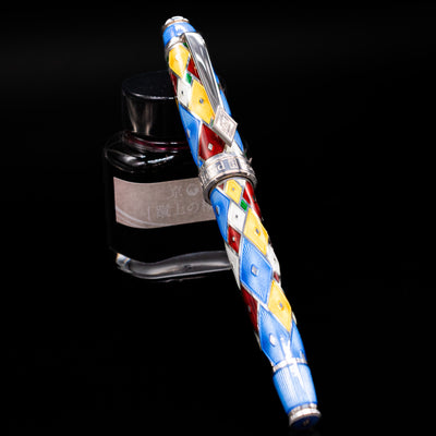 David Oscarson Harlequin Fountain Pen - Sapphire Blue capped, leaning against an ink bottle. 