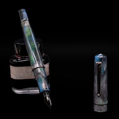 Delta Duna Fountain Pen - Zephyr leaning on an ink bottle uncapped showcasing the detailing on the nib.