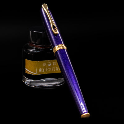 Diplomat Excellence A2 Fountain Pen - Deep Purple capped, leaning against an ink bottle.